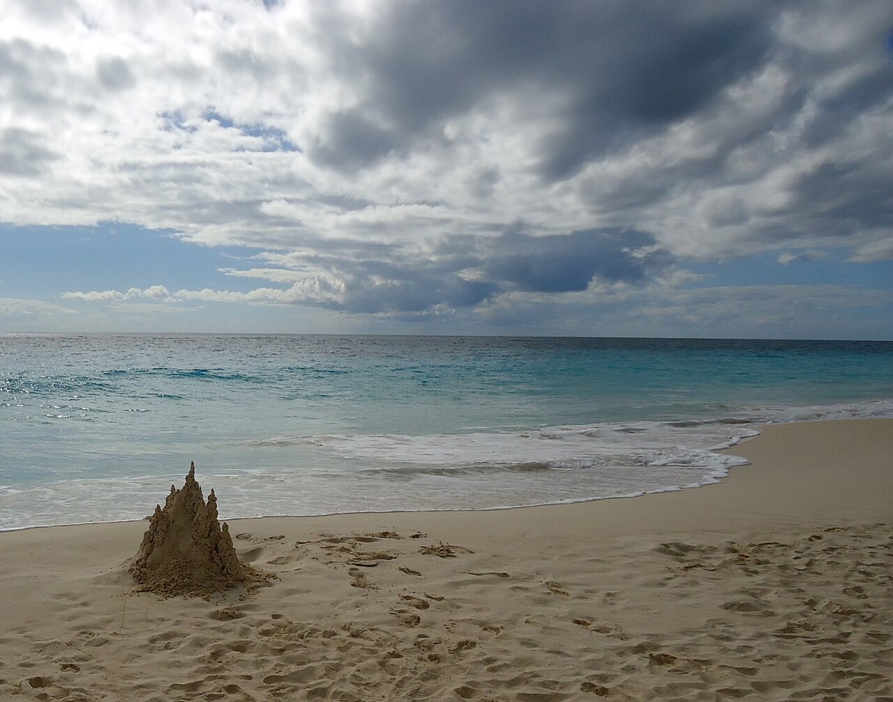 A sandcastle on a beach with clouds over the Atlantic Ocean.