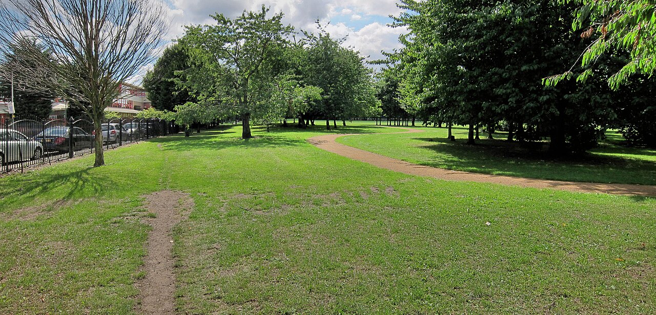 A wriggly paved path beside a straight worn desire line cutting across the grass.
